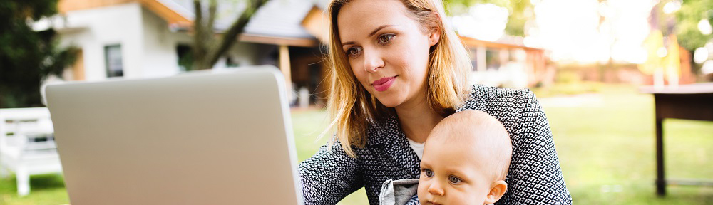 Photo of a young woman with a baby studying outdoors. A mother with laptop in the garden.