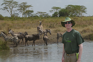 Instructor Greg Hervey poses at a watering hole with Zebras and other wild animals on one of his many trips.