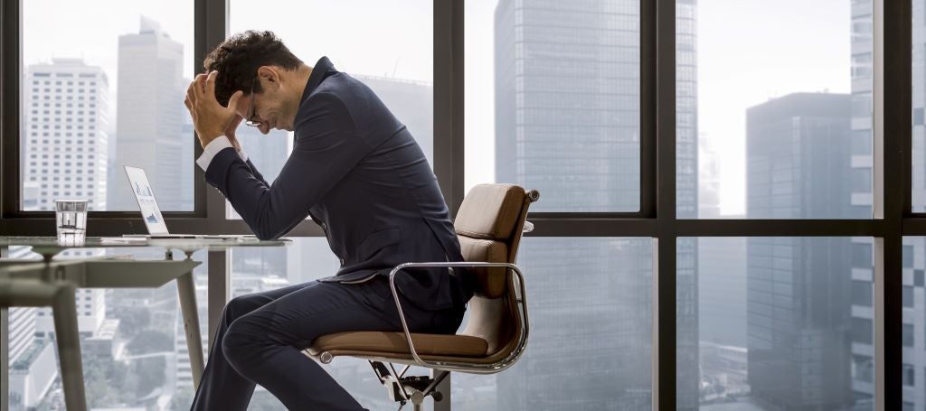 Business man sits at end of conference table with his head in his hands